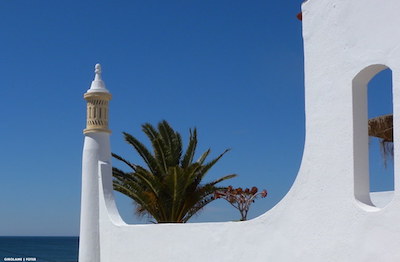 View across a villa with chimney to the sea with a palm and bougainvillea in the foreground