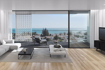 View across a living room through wall-to-wall folding glass doors to a balcony and sea view beyond