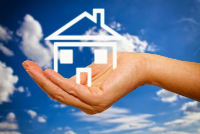 Hand holding outline of house with blue sky and clouds behind