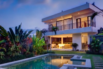 Villa with lights on at dusk in garden with swimming pool