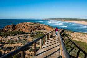 People walking down a boardwalk on a rugged algarve coastline