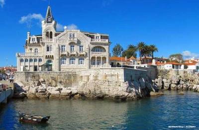 Large building on the water's edge with Portuguese fishing boat floating inf ront