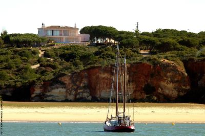 sHIP ANCHORED OFF A BEACH WITH A VILLA OVERLOOKING FROM THE CLIFFS