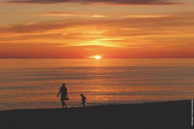 Adult and child walking at sunset on a beach