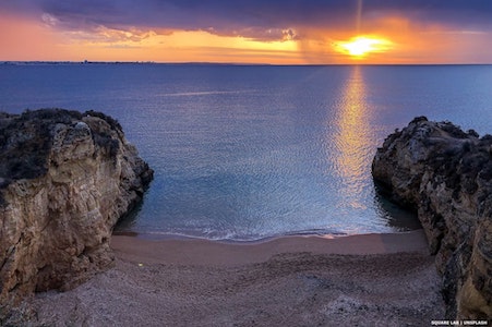View from cliffs across a beach to sunset over the sea