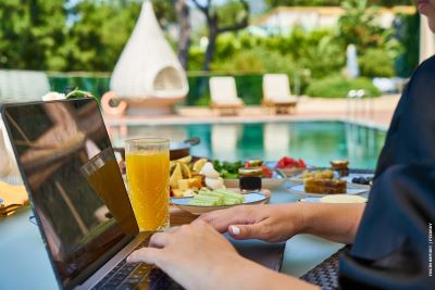 WORKING AT COMPUTER ON TABLE WITH BREAKFAST AROUND A SWIMMING POOL